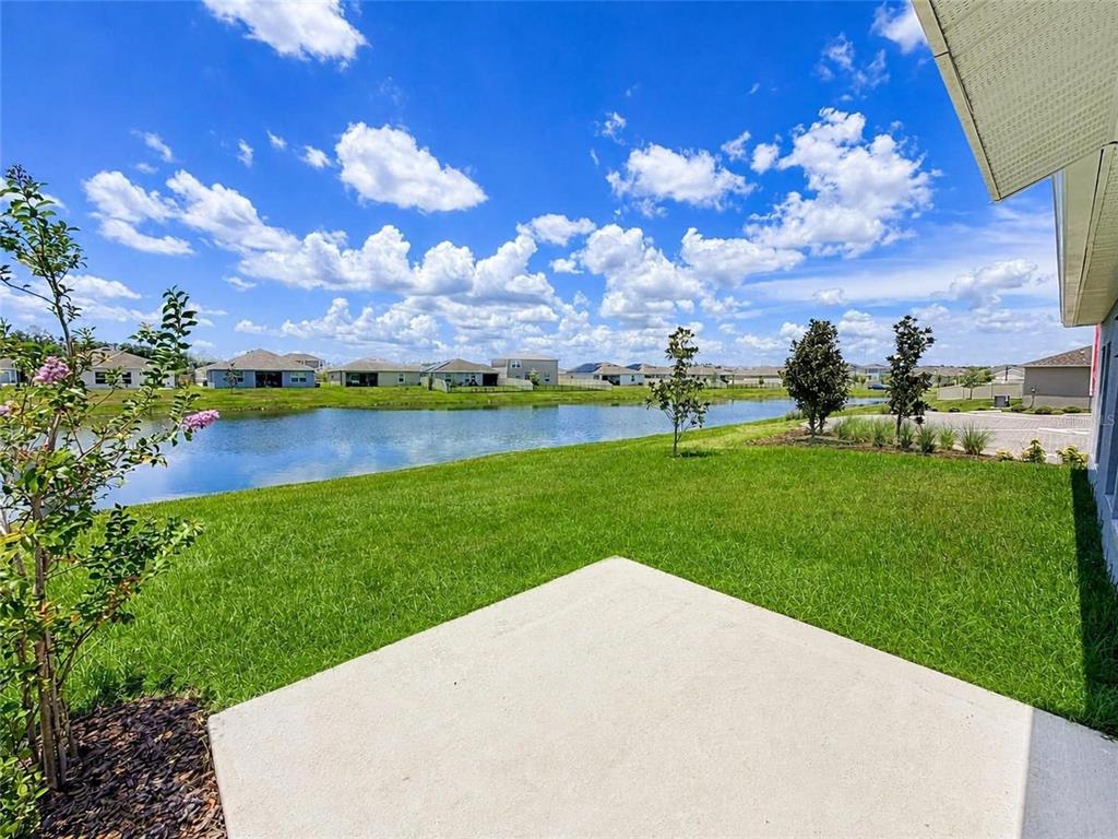 A concrete patio overlooks a grassy backyard and a pond with houses in the distance — 5638 LOGGIA LANE, KISSIMMEE, FL