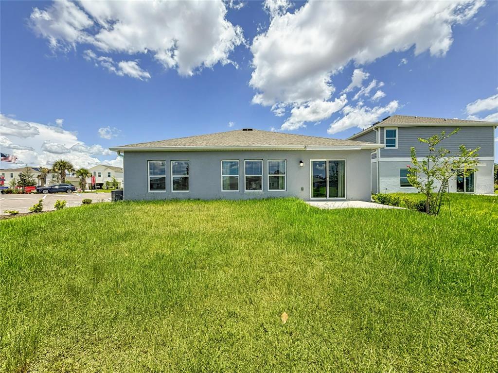 The rear exterior of a gray single-story house features a large grassy yard — 5638 LOGGIA LANE, KISSIMMEE, FL