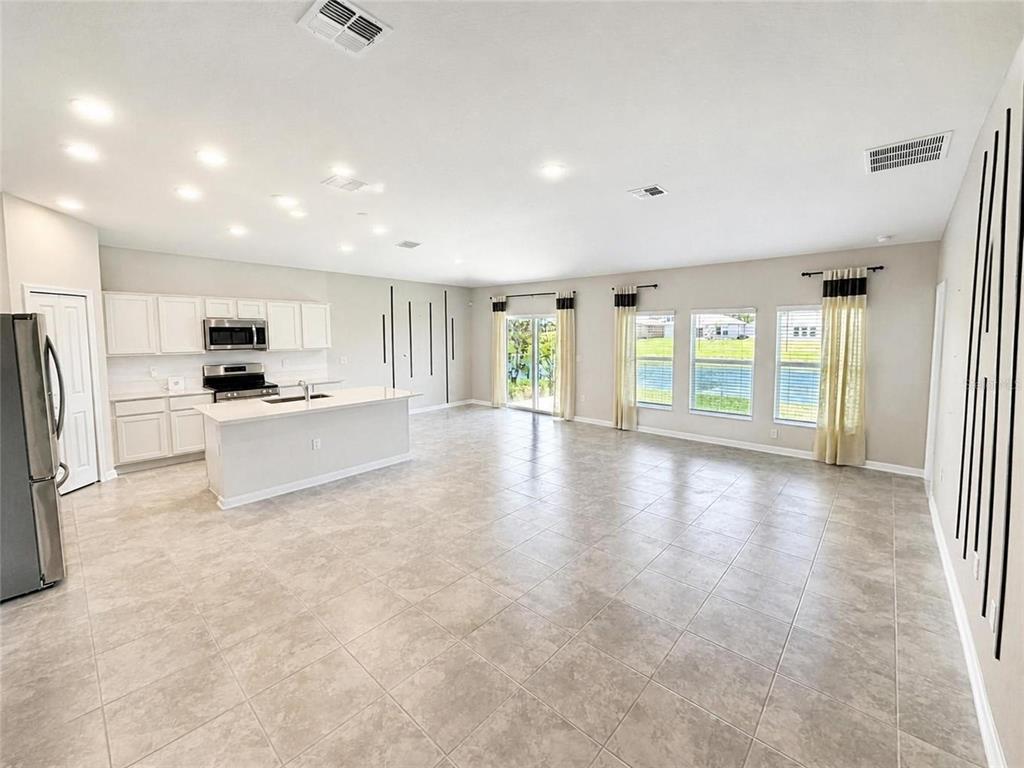 A kitchen with white cabinets and an island opens into a large, tiled living area — 5638 LOGGIA LANE, KISSIMMEE, FL