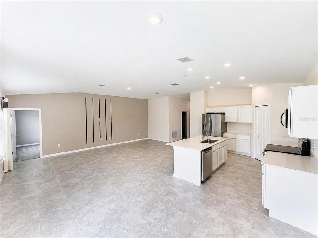 An open-concept kitchen and living area features light gray tile flooring and white cabinetry — 5638 LOGGIA LANE, KISSIMMEE, FL