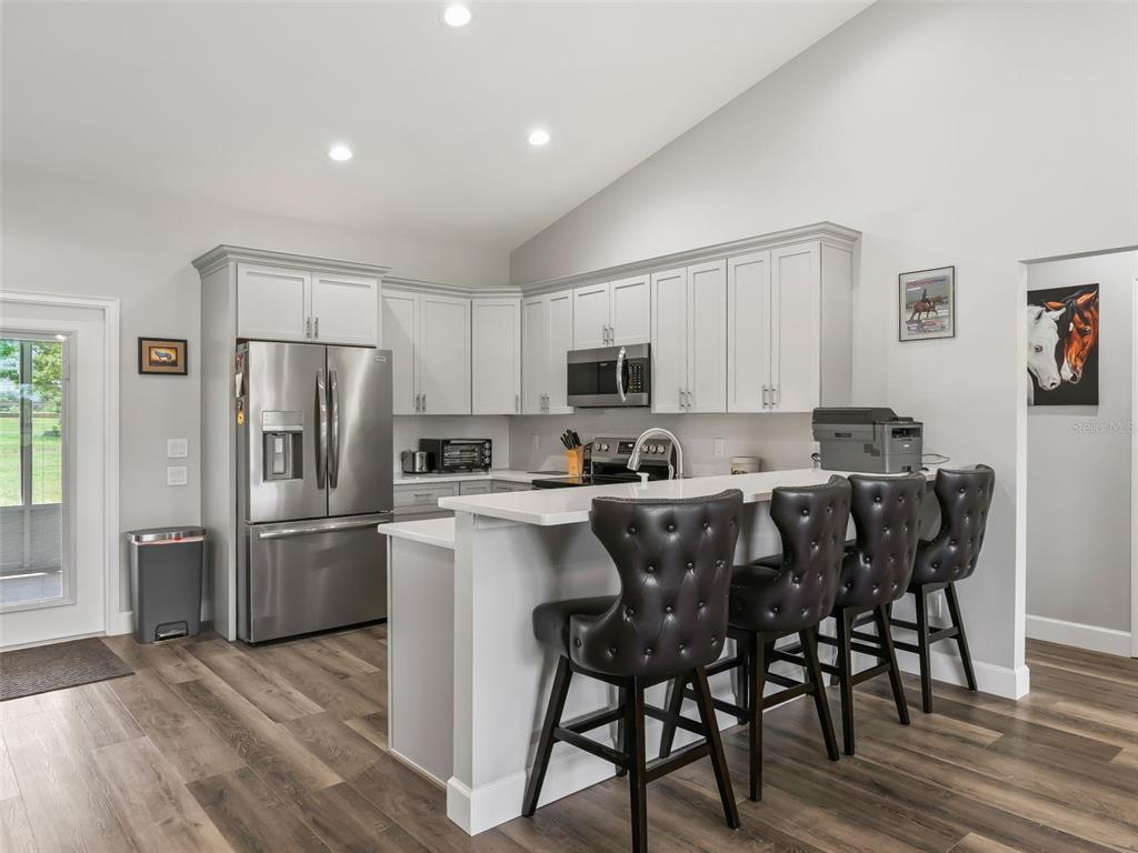 A kitchen features white cabinets, stainless steel appliances, a breakfast bar, and wood-look flooring — 1771 SE 119TH AVENUE, MORRISTON, FL