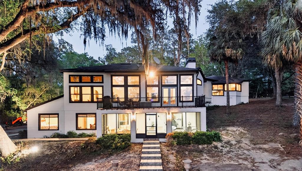 A two-story white house with black window frames and a balcony overlooks a sloped yard — 17704 SE 59TH STREET, MICANOPY, FL