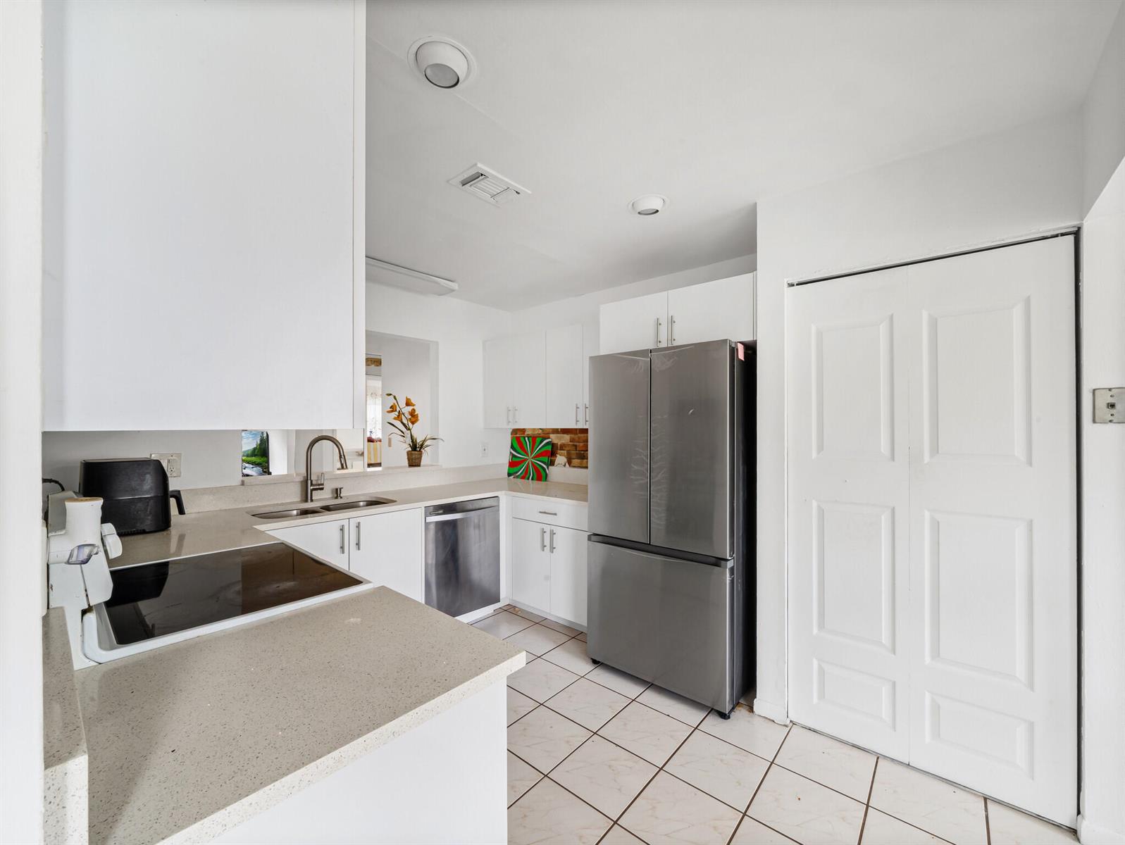 A kitchen features white cabinets, stainless steel appliances, light countertops, and white tile flooring — 6292 Silver Moon Lane, FL 33463, FL
