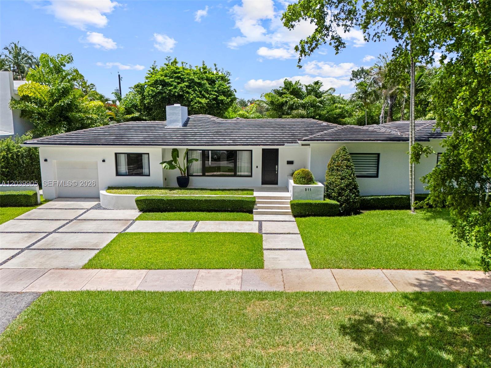 A white single-story house features a dark tiled roof, a garage, and manicured landscaping — 511 Perugia Ave, Coral Gables FL 33146, CORAL GABLES, FL