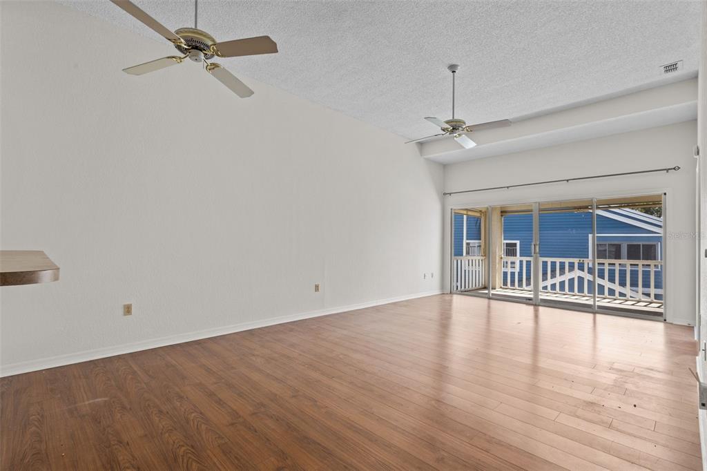 An empty living room with wood-look flooring, two ceiling fans, and sliding glass patio doors — 2014 GOLFVIEW DRIVE UNIT 2014, TARPON SPRINGS, FL