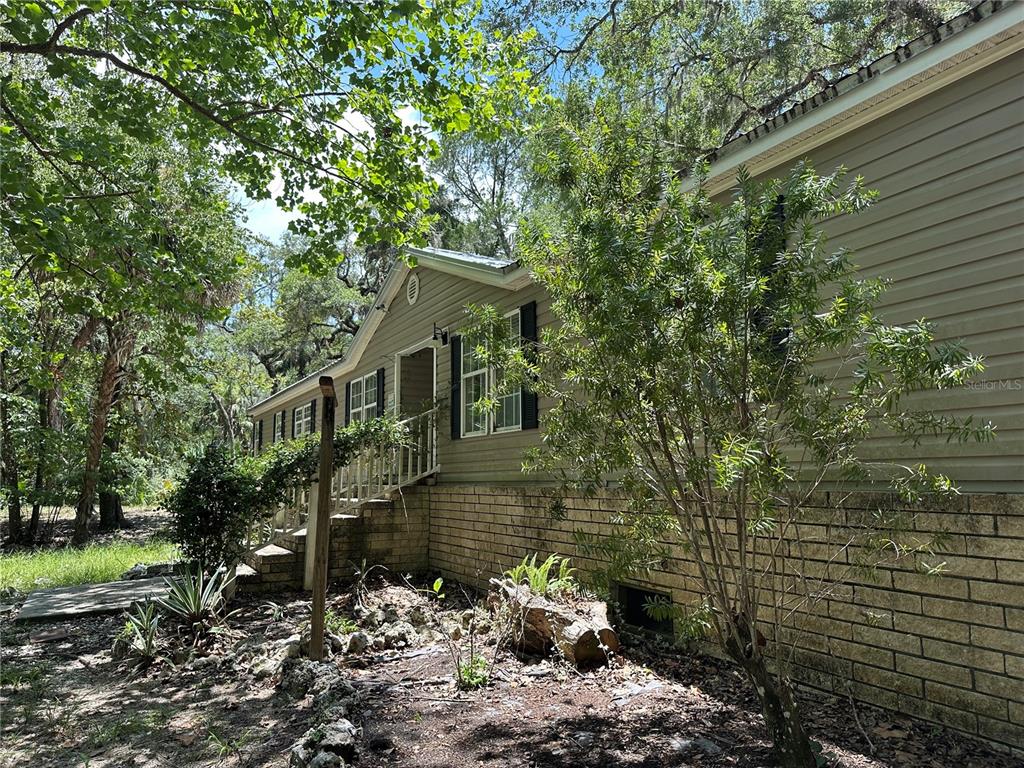 A tan house with a brick foundation sits in a wooded area with trees — 292 S DEW PLANT POINT, CRYSTAL RIVER, FL