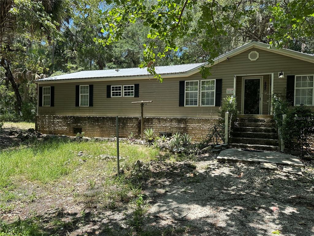 A single-story house with tan siding and a brick foundation sits in a wooded area — 292 S DEW PLANT POINT, CRYSTAL RIVER, FL
