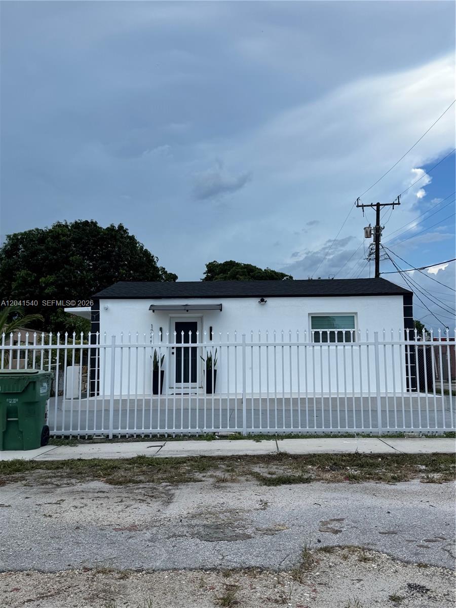 A white, single-story house with a black roof sits behind a white metal fence — 1245 Vermont St, Opa-Locka FL 33054, OPA-LOCKA, FL
