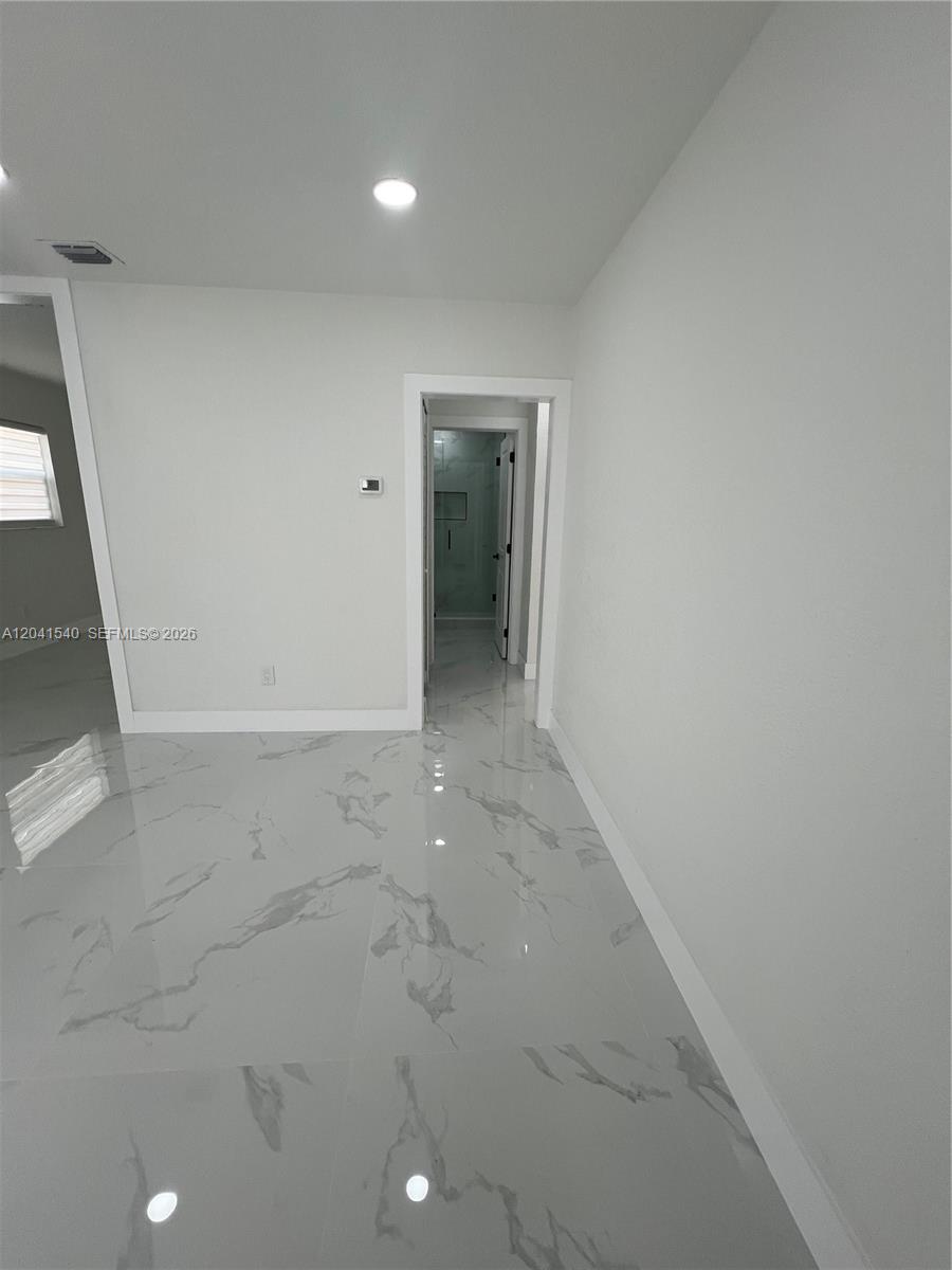 A room with white walls and glossy, light-colored marble-patterned tile flooring leads to a doorway — 1245 Vermont St, Opa-Locka FL 33054, OPA-LOCKA, FL