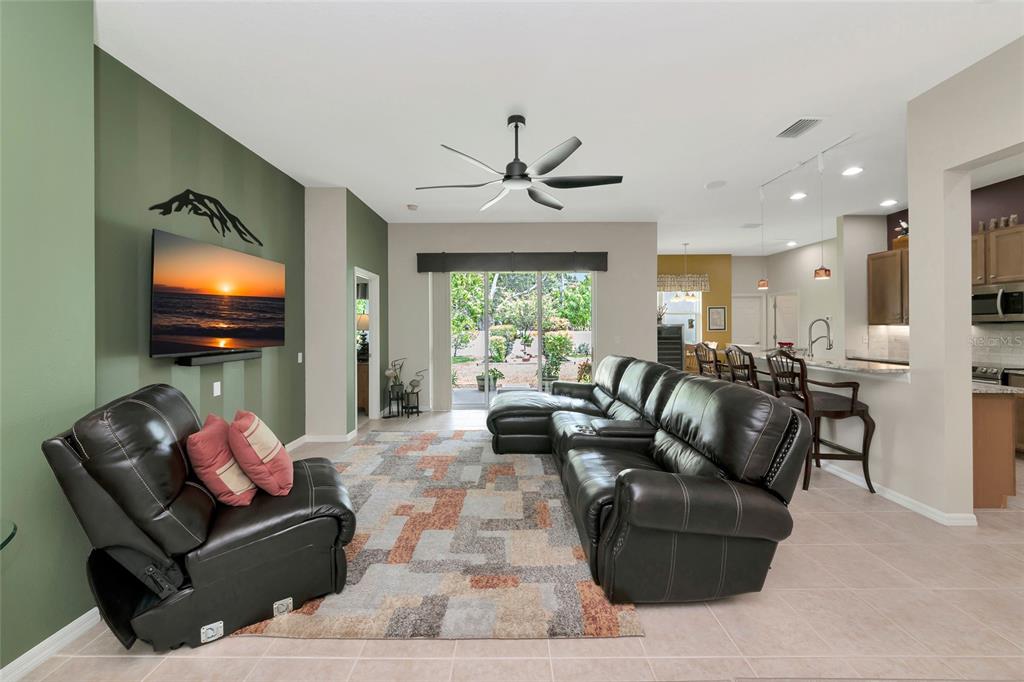 A living room with a green accent wall, dark leather furniture, and an open kitchen — 5720 43RD COURT E, BRADENTON, FL
