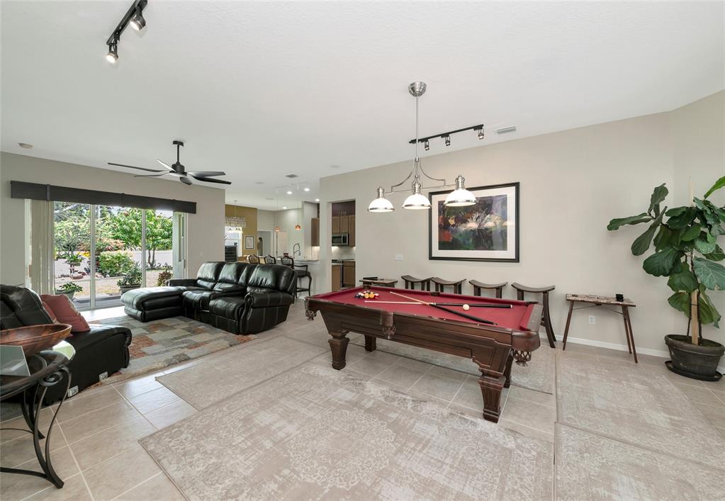 A living room with a pool table, leather sectional, and tile flooring opens to a patio — 5720 43RD COURT E, BRADENTON, FL
