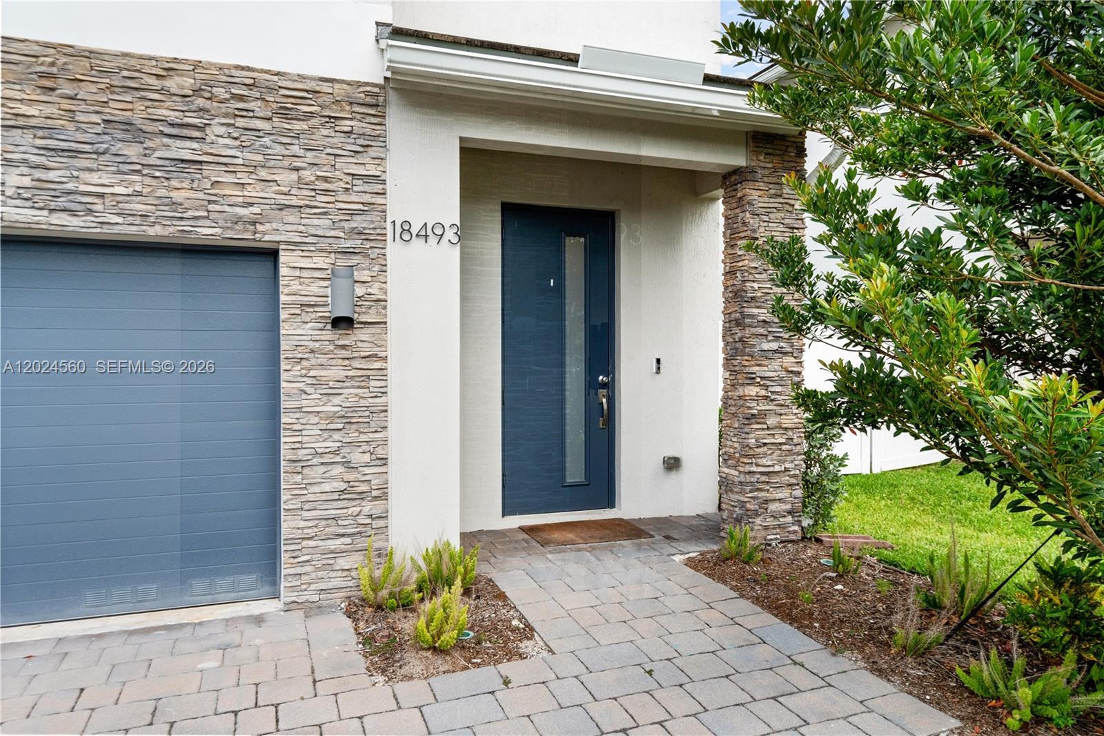 The exterior of a home features a stone facade, a blue garage door, and a matching front door — 18493 Glenstone St, Jupiter FL 33458, JUPITER, FL
