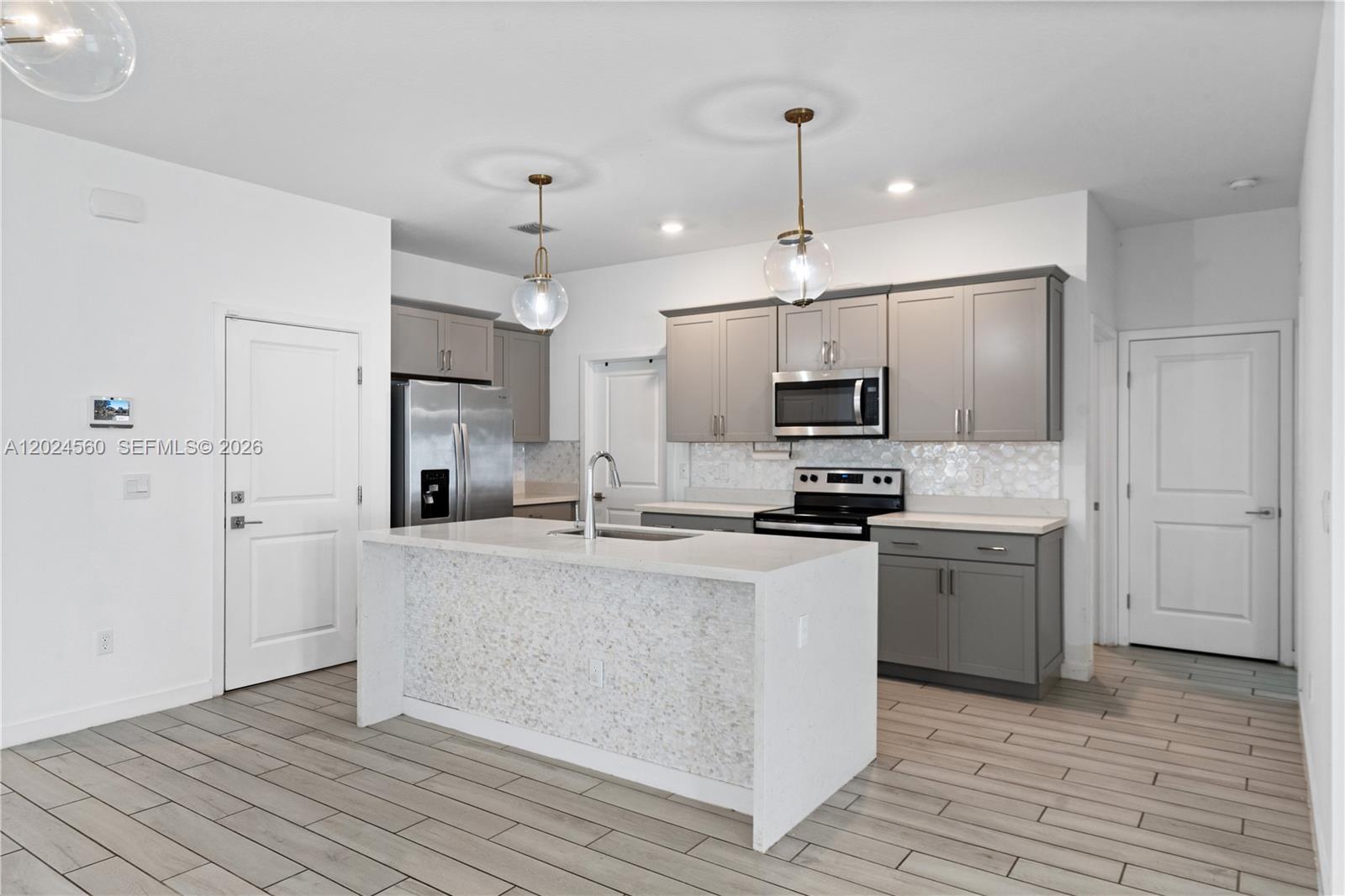 A modern kitchen features gray cabinets, a white quartz island, and light wood-look flooring — 18493 Glenstone St, Jupiter FL 33458, JUPITER, FL