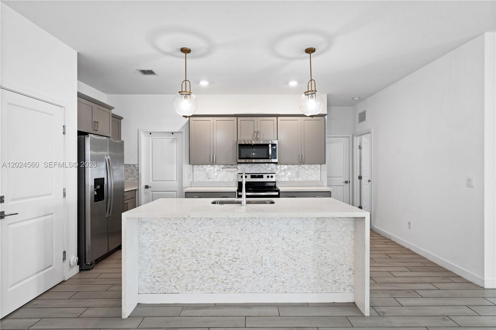 A modern kitchen features a central island, grey cabinetry, stainless steel appliances, and tile flooring — 18493 Glenstone St, Jupiter FL 33458, JUPITER, FL