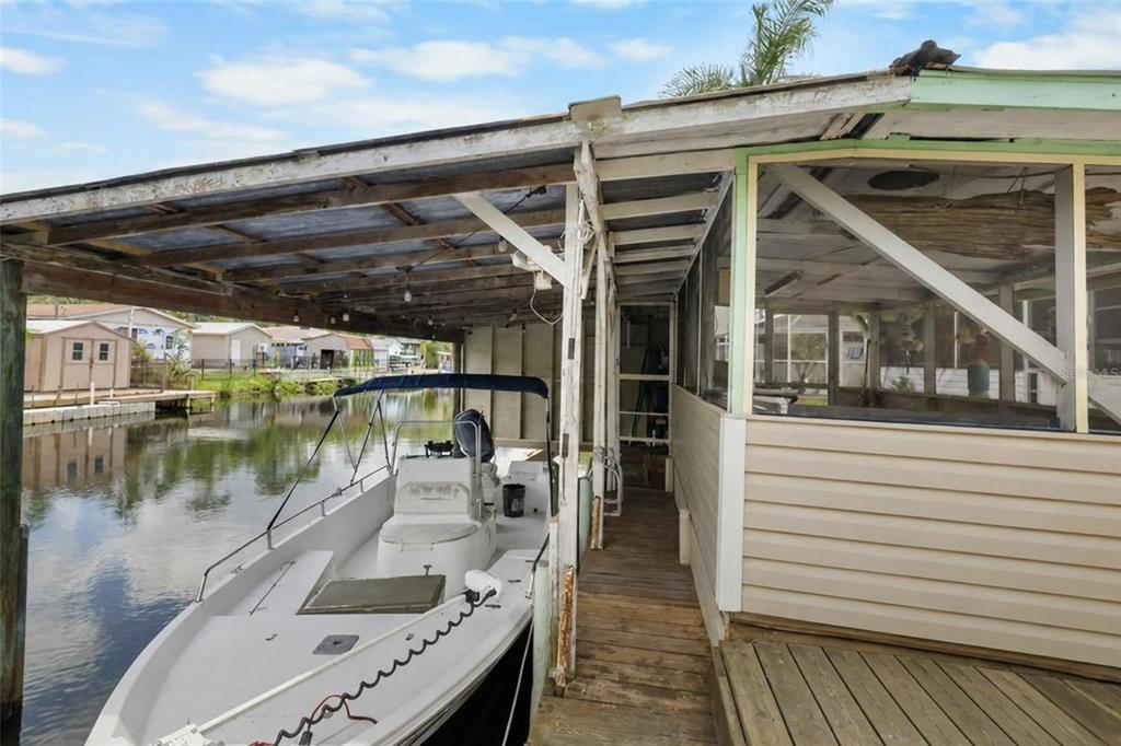 A boat is docked under a covered slip next to a screened-in porch — 7264 ABERDEEN COURT, WEEKI WACHEE, FL