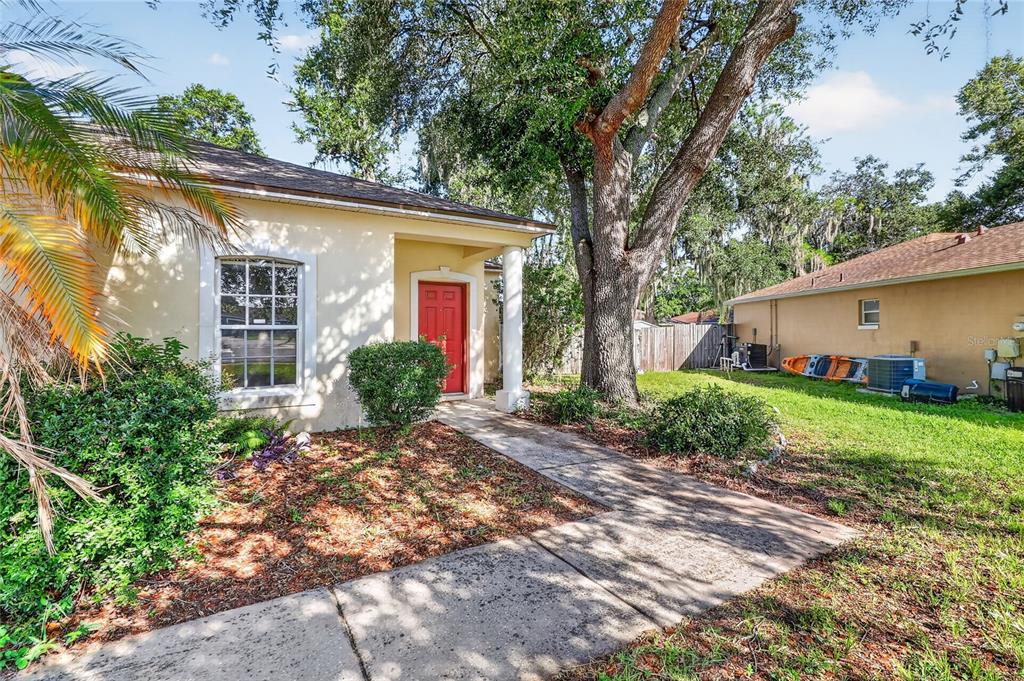 A tan house with a red front door, a concrete walkway, and a large oak tree — 2614 SUNDANCE COURT, MULBERRY, FL