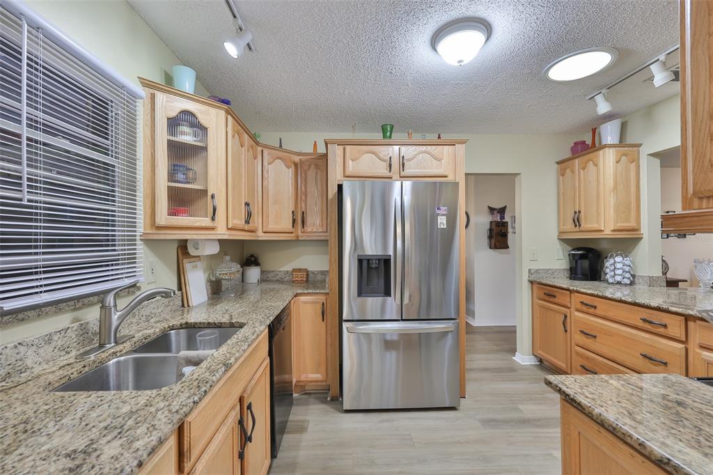 A kitchen features light wood cabinets, granite countertops, stainless steel appliances, and a double sink — 1511 CLOISTER DRIVE, SUN CITY CENTER, FL