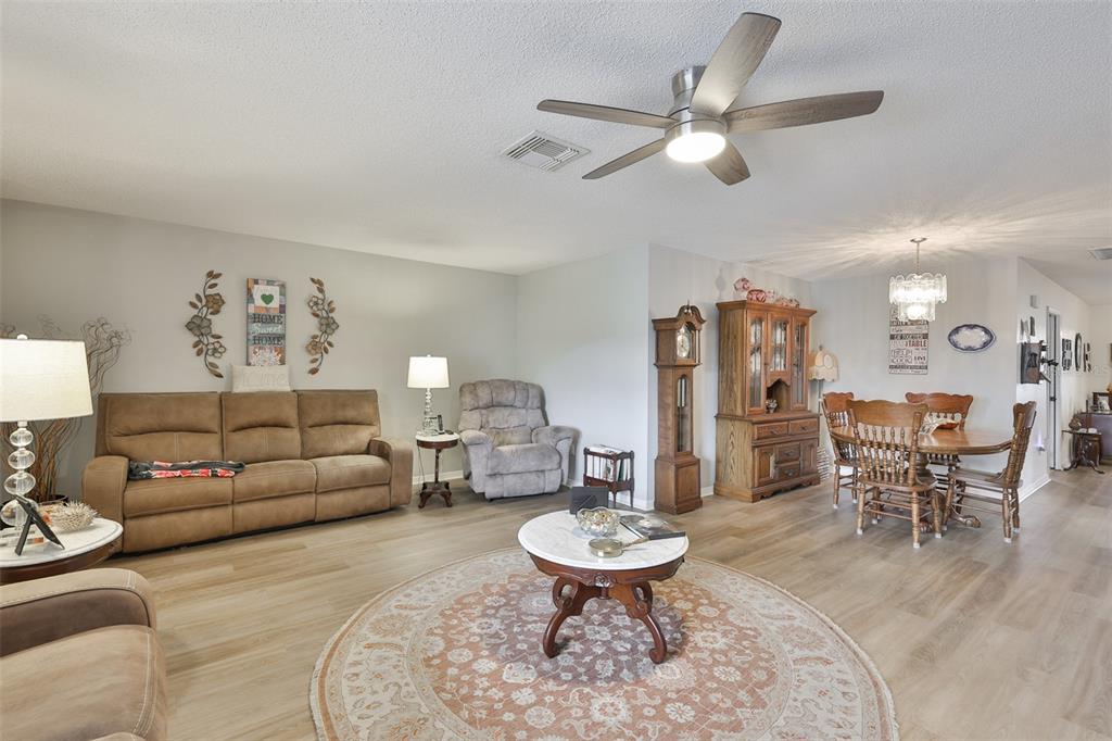 A living and dining room area features light wood flooring, a ceiling fan, and furniture — 1511 CLOISTER DRIVE, SUN CITY CENTER, FL