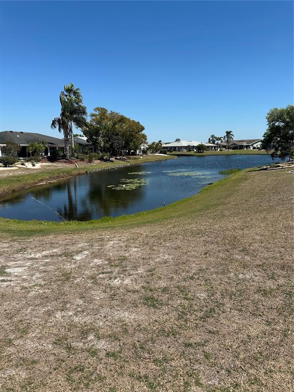 A pond sits between residential houses and a grassy lawn under a clear blue sky — 1511 CLOISTER DRIVE, SUN CITY CENTER, FL