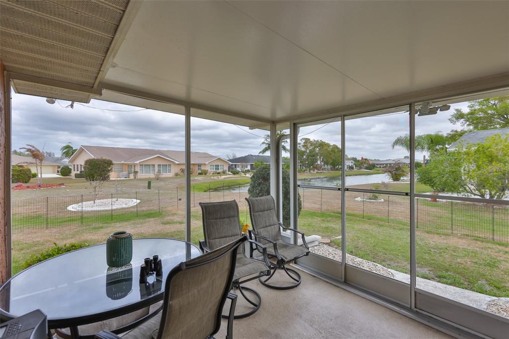 A screened-in patio with a glass-top table and chairs overlooking a backyard and pond — 1511 CLOISTER DRIVE, SUN CITY CENTER, FL