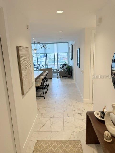 A hallway with marble-look tile flooring leads to an open-concept living area with floor-to-ceiling windows — 777 3RD AVENUE N UNIT 1007, ST PETERSBURG, FL