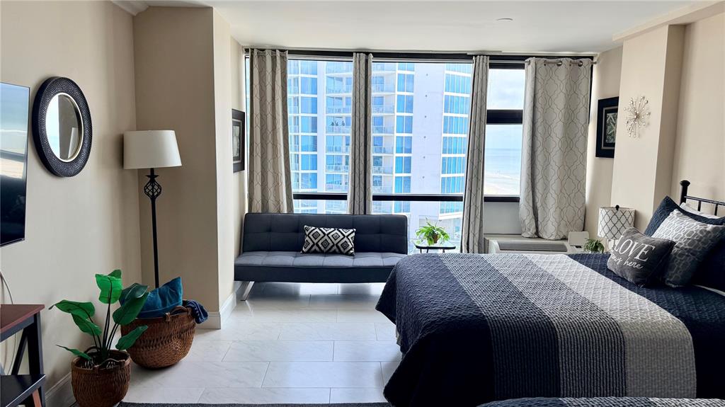 A bedroom with a bed, sofa, and floor-to-ceiling windows overlooking a beach and buildings — 1909 S ATLANTIC AVENUE UNIT 621, DAYTONA BEACH, FL