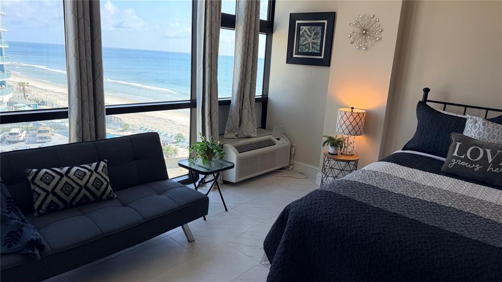 A bedroom features a bed, a sofa, and floor-to-ceiling windows overlooking the ocean — 1909 S ATLANTIC AVENUE UNIT 621, DAYTONA BEACH, FL