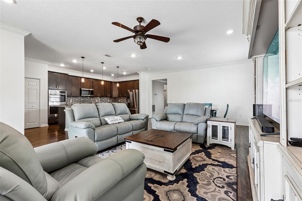 A living room features light gray leather sofas, a wooden coffee table, and an open kitchen — 8245 OLIVE BROOK DRIVE, WESLEY CHAPEL, FL