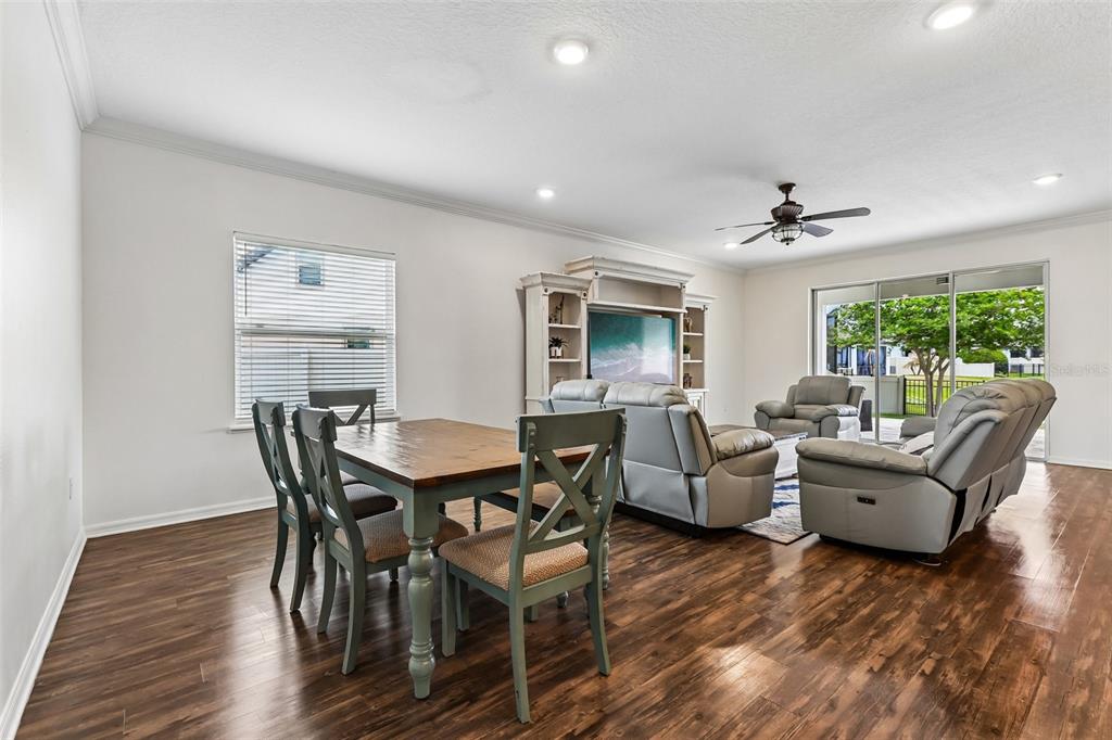 A dining area and living room feature wood-look flooring, gray furniture, and sliding glass doors — 8245 OLIVE BROOK DRIVE, WESLEY CHAPEL, FL