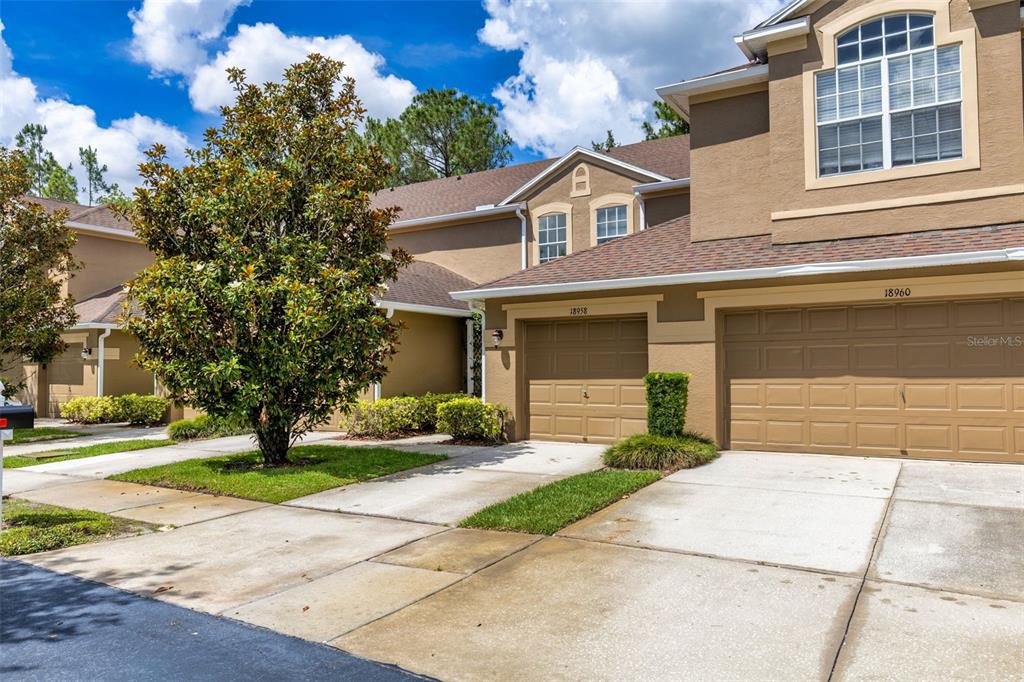 The exterior of two attached townhomes features tan stucco walls, brown shingle roofs, and garages — 18958 DUQUESNE DRIVE, TAMPA, FL