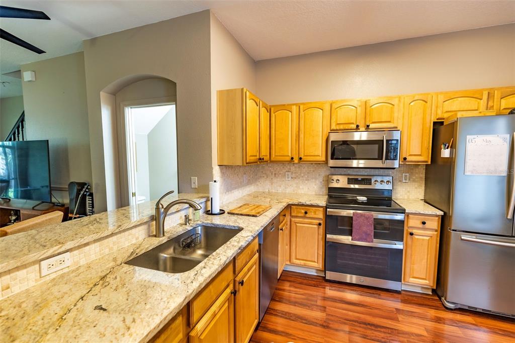 A kitchen features light wood cabinets, granite countertops, stainless steel appliances, and wood flooring — 18958 DUQUESNE DRIVE, TAMPA, FL