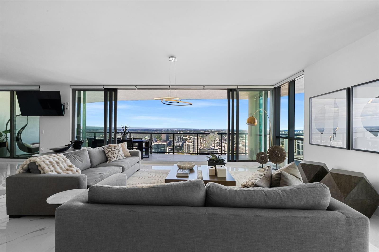 A modern living room features gray sofas, a coffee table, and floor-to-ceiling windows with city views — 100 E Las Olas Boulevard # 4001, Fort Lauderdale FL 33301, FORT LAUDERDALE, FL