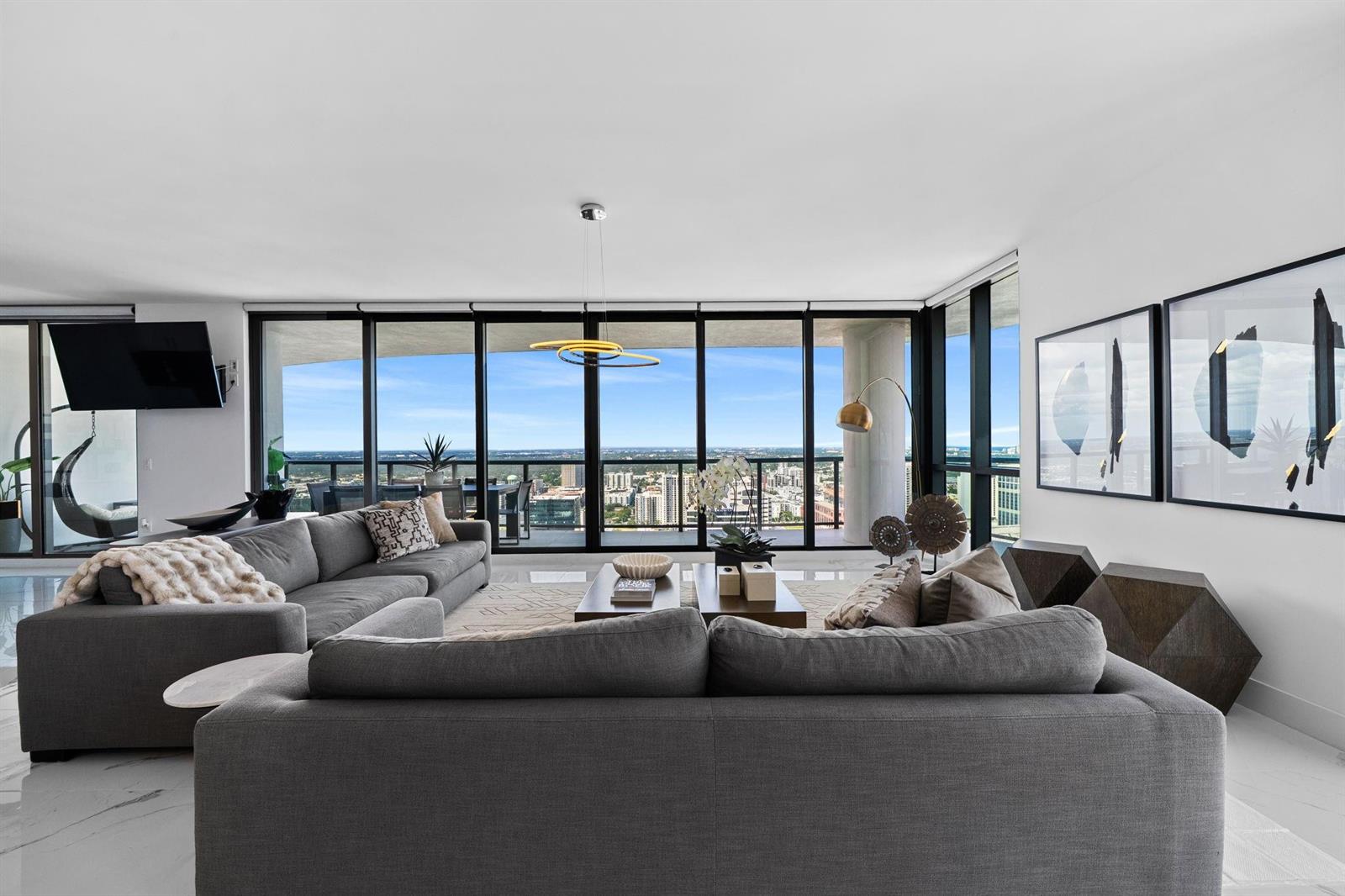 A modern living room features a grey sectional sofa, floor-to-ceiling windows, and city views — 100 E Las Olas Boulevard # 4001, Fort Lauderdale FL 33301, FORT LAUDERDALE, FL