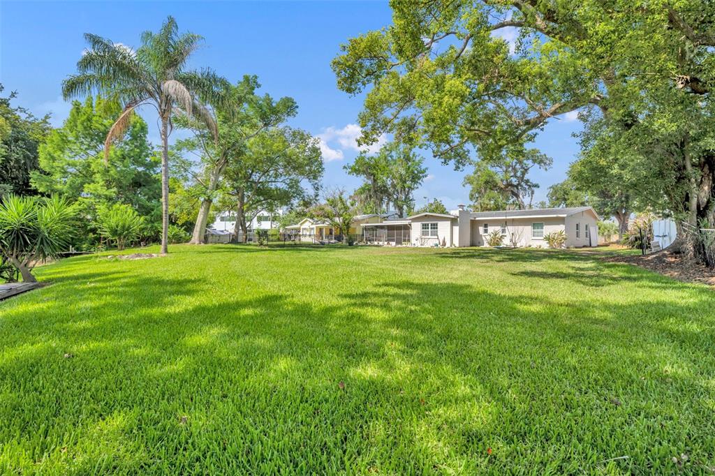 A large grassy backyard features mature trees, a palm tree, and a single-story house — 1009 LAKE BELL DRIVE, WINTER PARK, FL