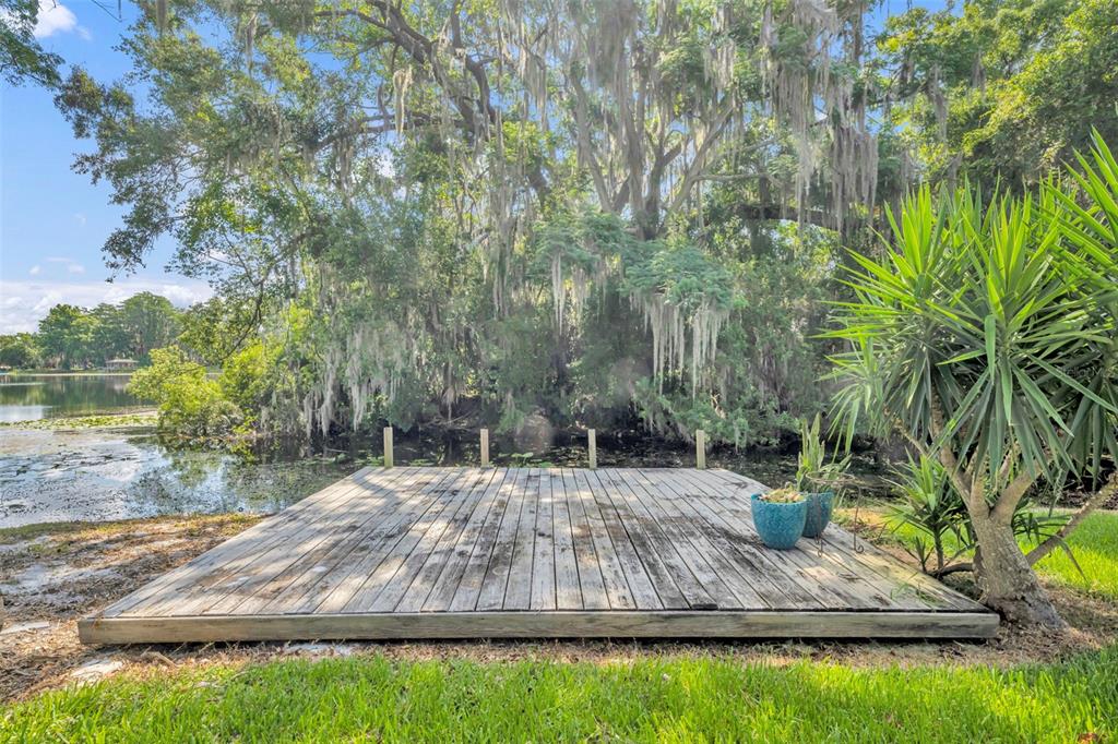 A wooden deck sits on the edge of a lake surrounded by trees with Spanish moss — 1009 LAKE BELL DRIVE, WINTER PARK, FL