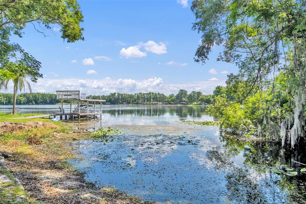 A wooden boat dock extends into a calm lake surrounded by trees under a blue sky — 1009 LAKE BELL DRIVE, WINTER PARK, FL