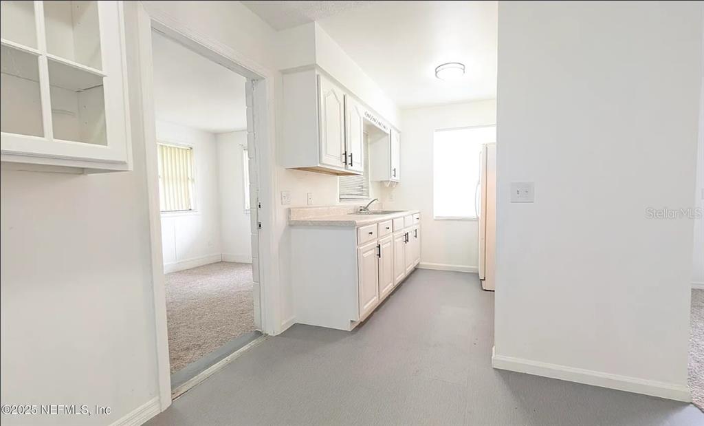 A kitchen with white cabinets, light countertops, and grey flooring leads into a carpeted room — 462 SALLY STREET, GREEN COVE SPRINGS, FL