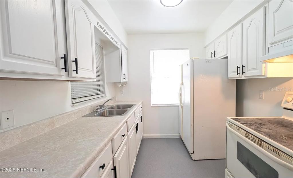 A galley-style kitchen features white cabinets, a double sink, and white appliances — 462 SALLY STREET, GREEN COVE SPRINGS, FL