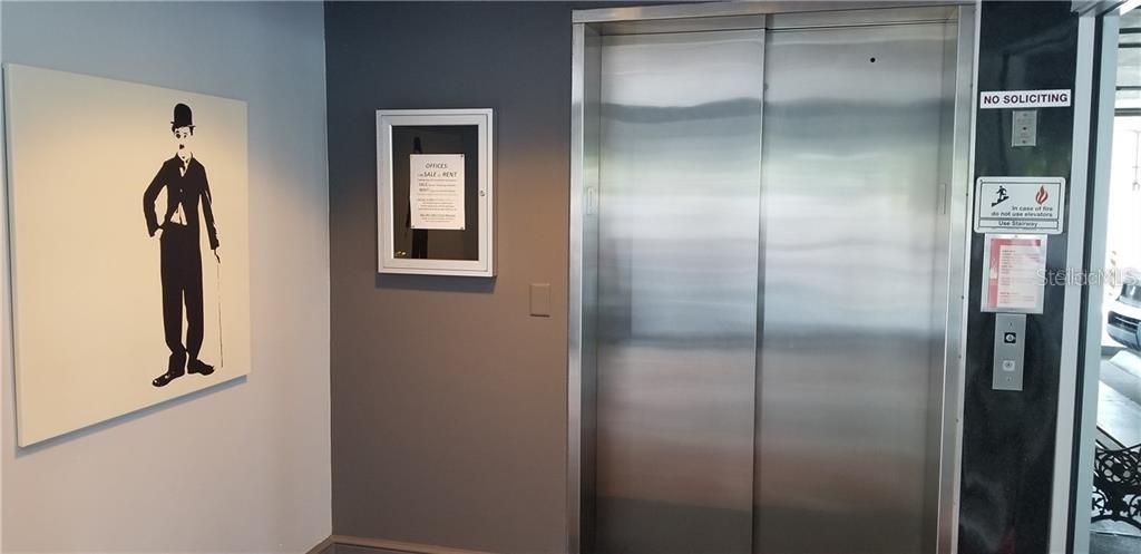 An elevator with stainless steel doors stands next to a Charlie Chaplin wall art piece — 7345 W SAND LAKE ROAD UNIT 307, ORLANDO, FL