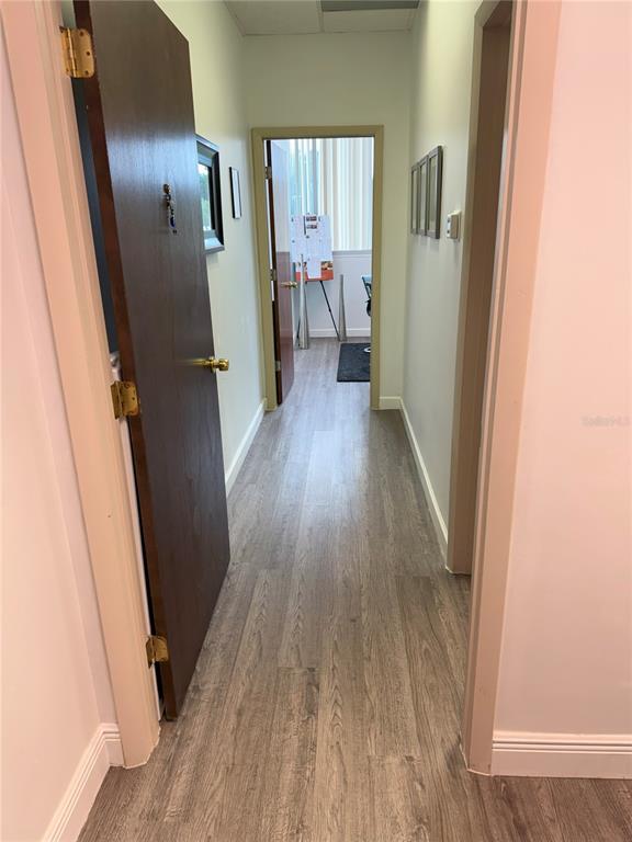 A hallway with wood-look flooring leads to an office space with a whiteboard — 7345 W SAND LAKE ROAD UNIT 307, ORLANDO, FL