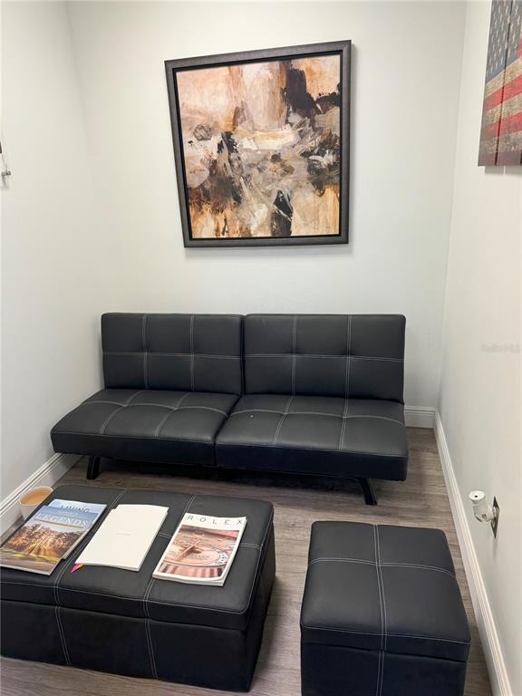 A small room features a black futon, a matching storage ottoman, and abstract wall art — 7345 W SAND LAKE ROAD UNIT 307, ORLANDO, FL