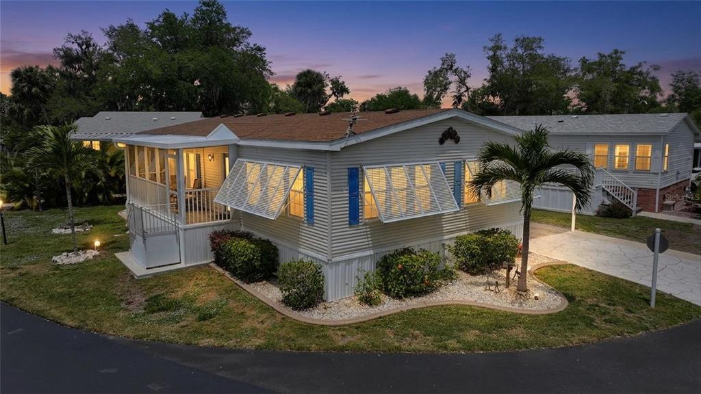 A single-story manufactured home with a screened porch, white siding, and blue shutters at dusk — 10303 BURNT STORE ROAD UNIT 143, PUNTA GORDA, FL
