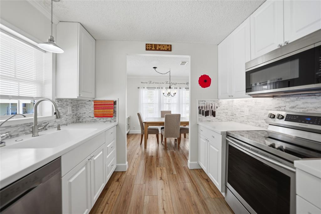 A bright kitchen with white cabinets, stainless steel appliances, and wood-look flooring leads to a dining area — 10303 BURNT STORE ROAD UNIT 143, PUNTA GORDA, FL