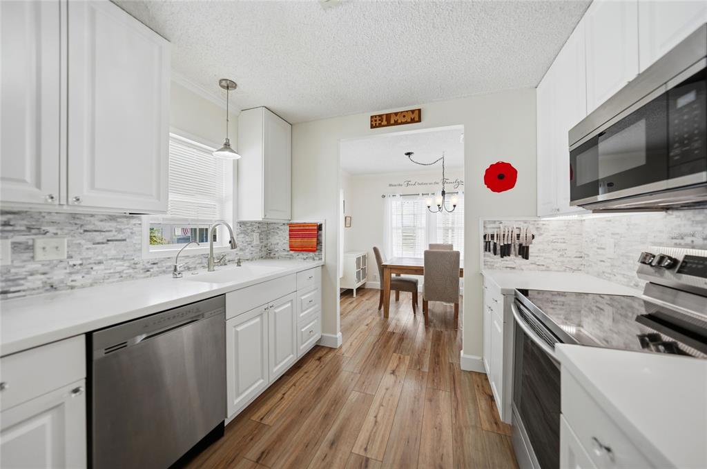 A white kitchen features stainless steel appliances, a tiled backsplash, and wood-look flooring — 10303 BURNT STORE ROAD UNIT 143, PUNTA GORDA, FL