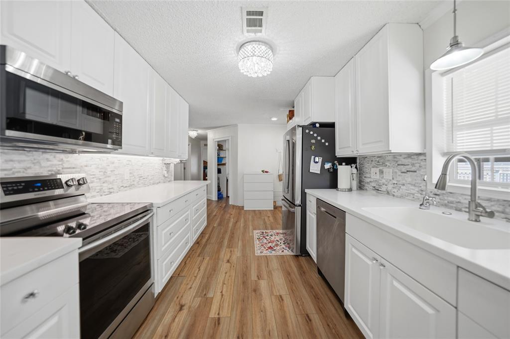 A galley kitchen features white cabinets, stainless steel appliances, a tiled backsplash, and wood flooring — 10303 BURNT STORE ROAD UNIT 143, PUNTA GORDA, FL