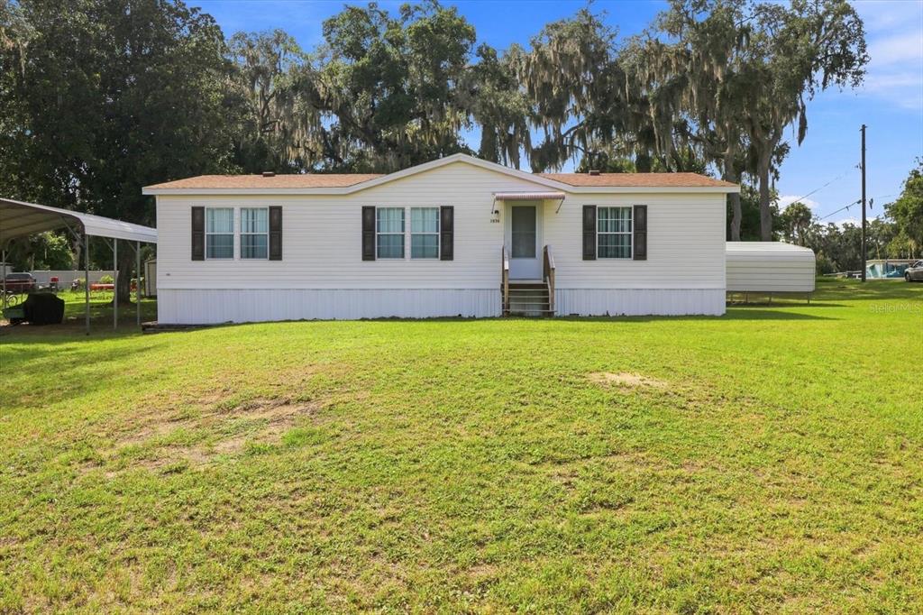A single-story manufactured home with white siding, dark shutters, and a metal carport — 2526 N LAKEFRONT DRIVE, HERNANDO, FL