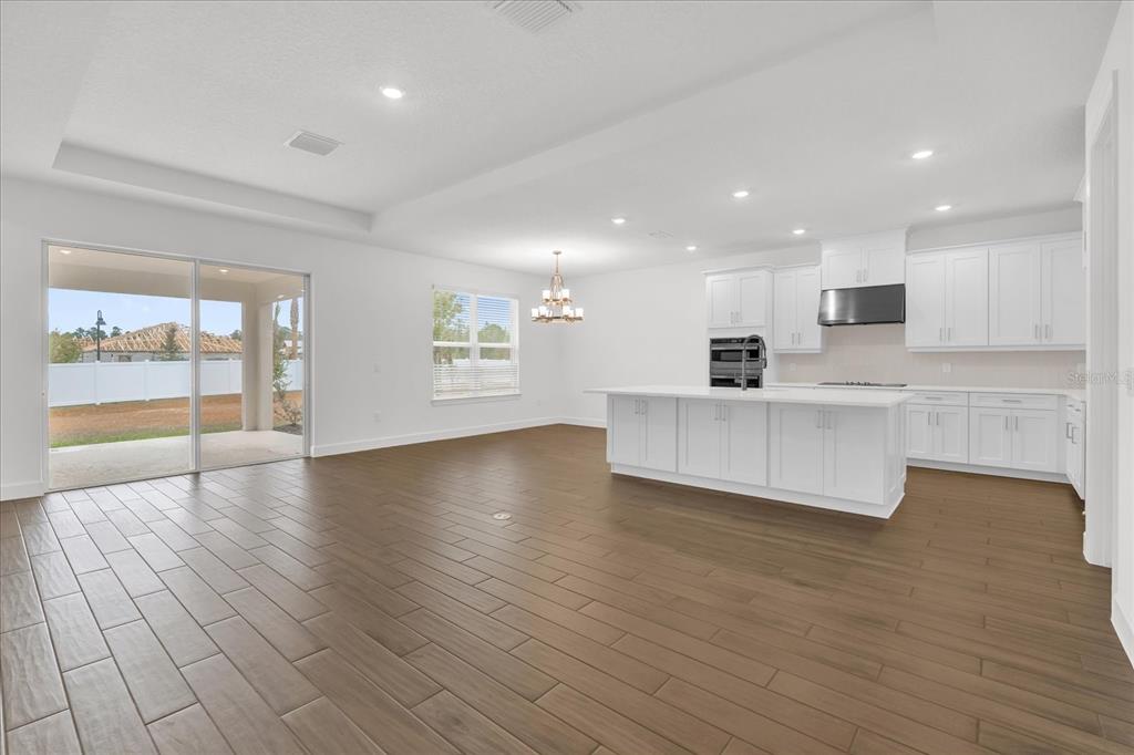 An open-concept kitchen and living area with white cabinetry, a large island, and wood-look flooring — 4246 BARBUDA LANE, KISSIMMEE, FL