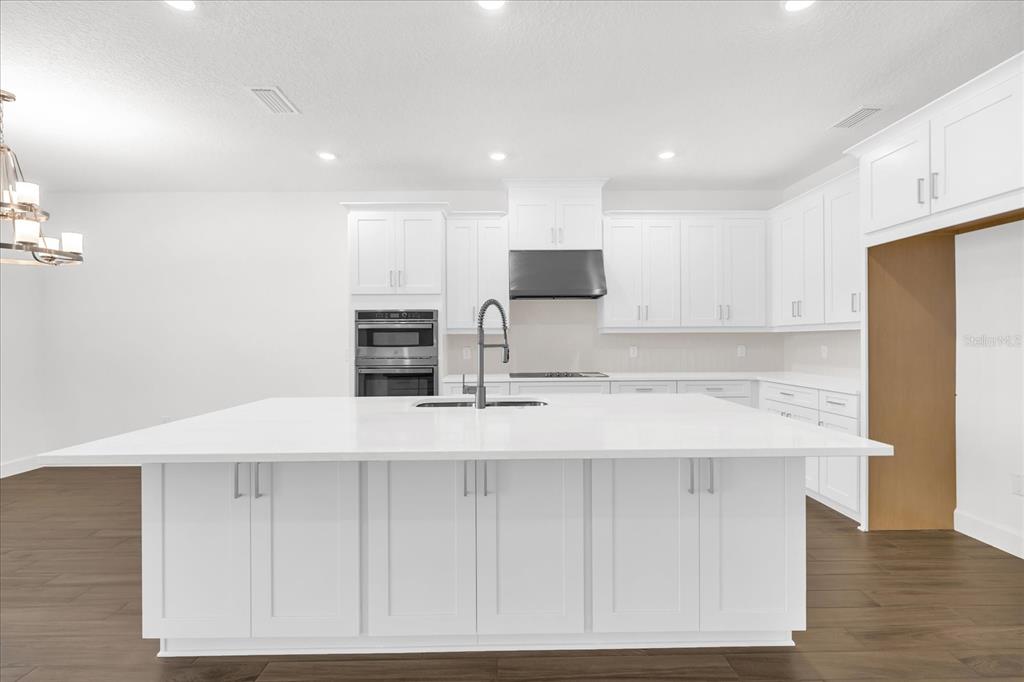 A modern kitchen features a large white island, white cabinetry, and stainless steel appliances — 4246 BARBUDA LANE, KISSIMMEE, FL