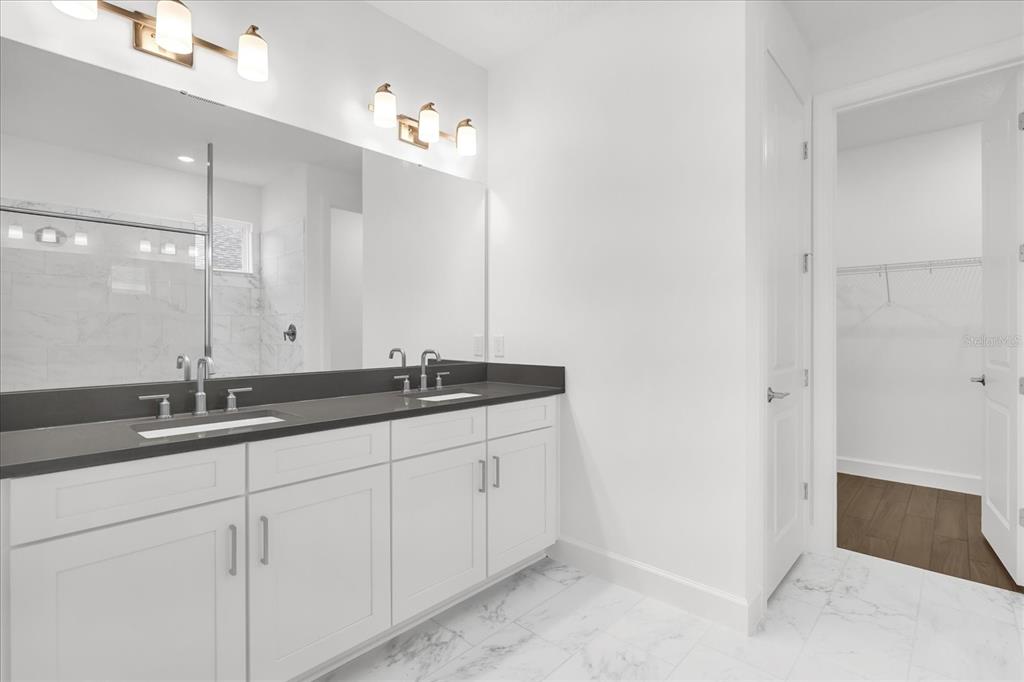 A modern bathroom features a double vanity with a dark countertop and white cabinetry — 4246 BARBUDA LANE, KISSIMMEE, FL