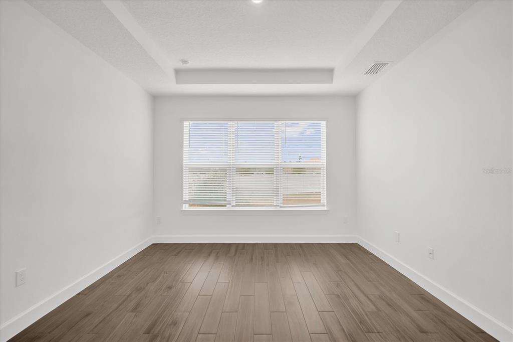An empty room with white walls, wood-look flooring, and a tray ceiling with a window — 4246 BARBUDA LANE, KISSIMMEE, FL